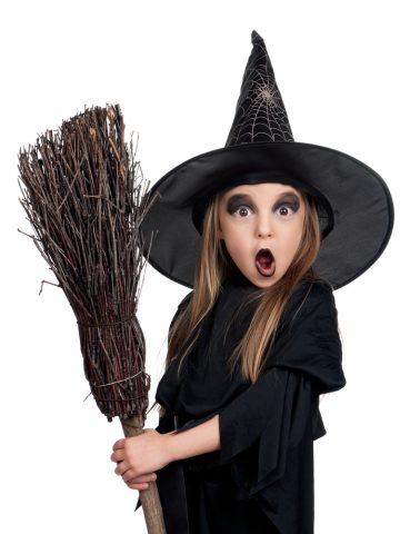 Portrait of little girl in black hat and black clothing with broom on white background