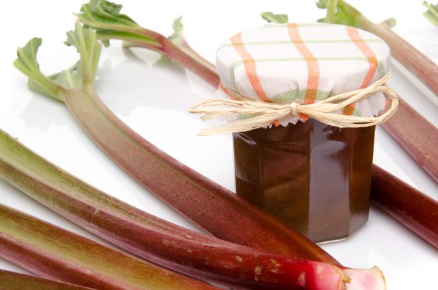 Jar of rhubarb jam with stalks of fresh rhubarb, isolated on white