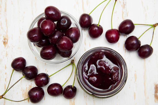 Cherry jam with fresh cherries on a wooden background