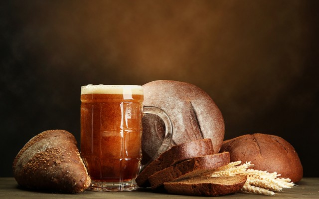 tankard of kvass and rye breads with ears, on wooden table on brown background