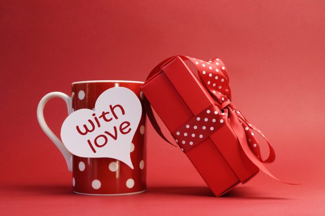 "With love" message on red polka dot mug and red gift with polka dot ribbon bow against a red background for a bright, fun and cheerful Valentines Day.